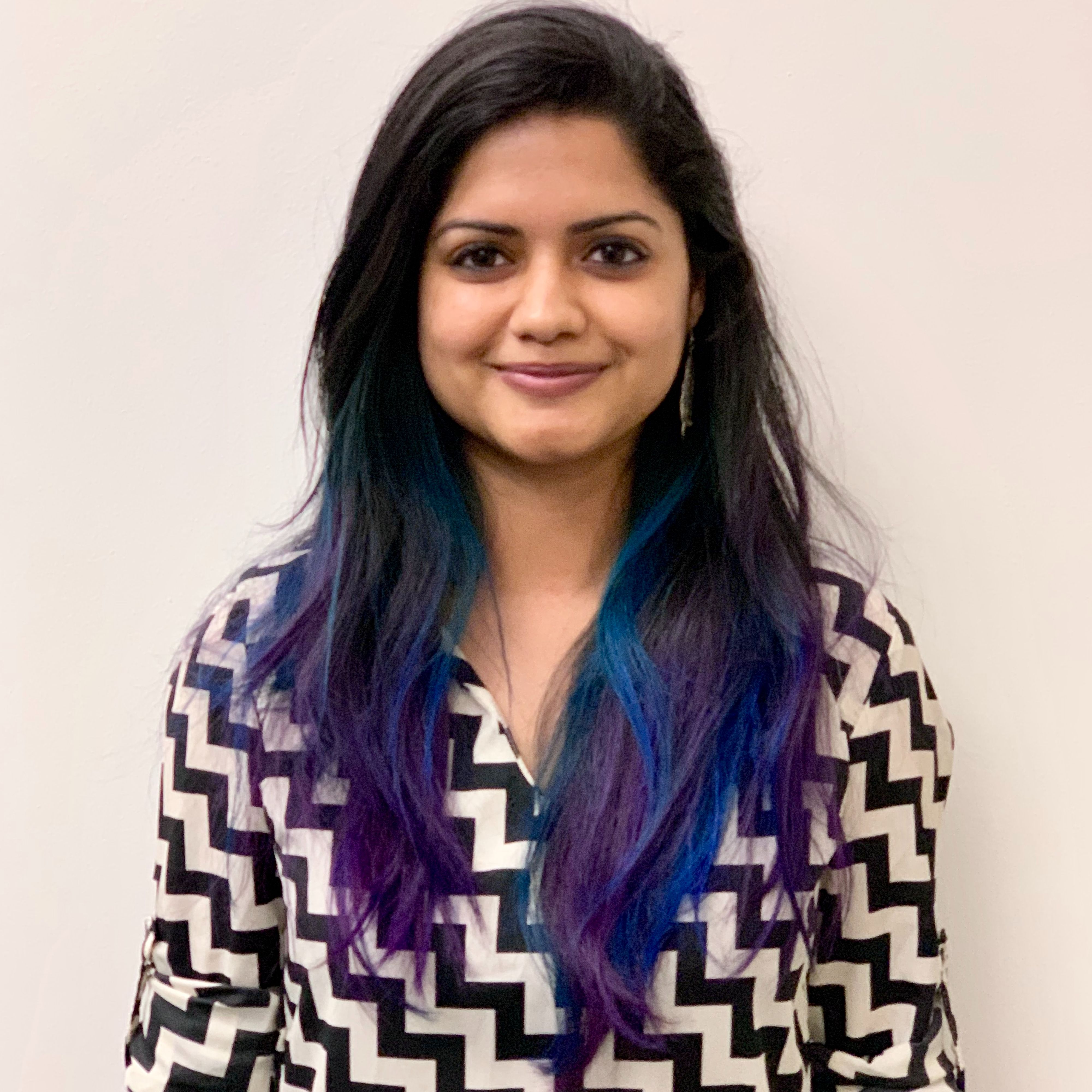 Kaush smiling, with striking blue and purple highlights at the bottom of her dark hair