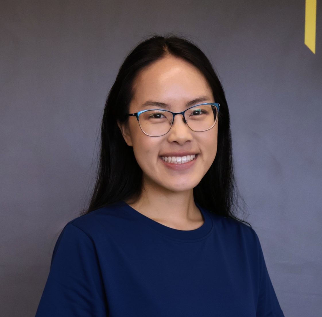 Maggie smiling, wearing blue glasses and a navy top